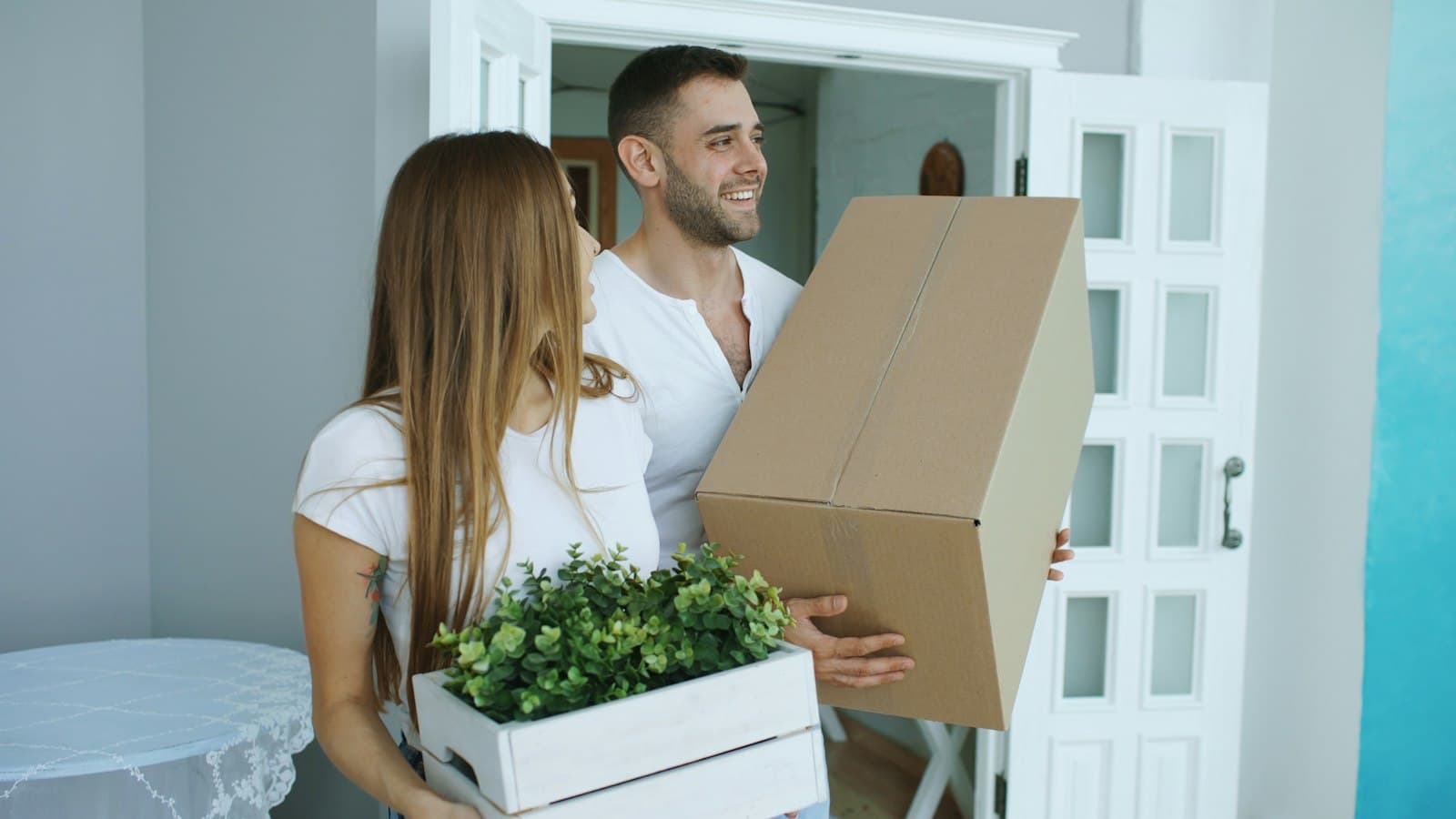 A couple carrying cardboard moving boxes into a new home