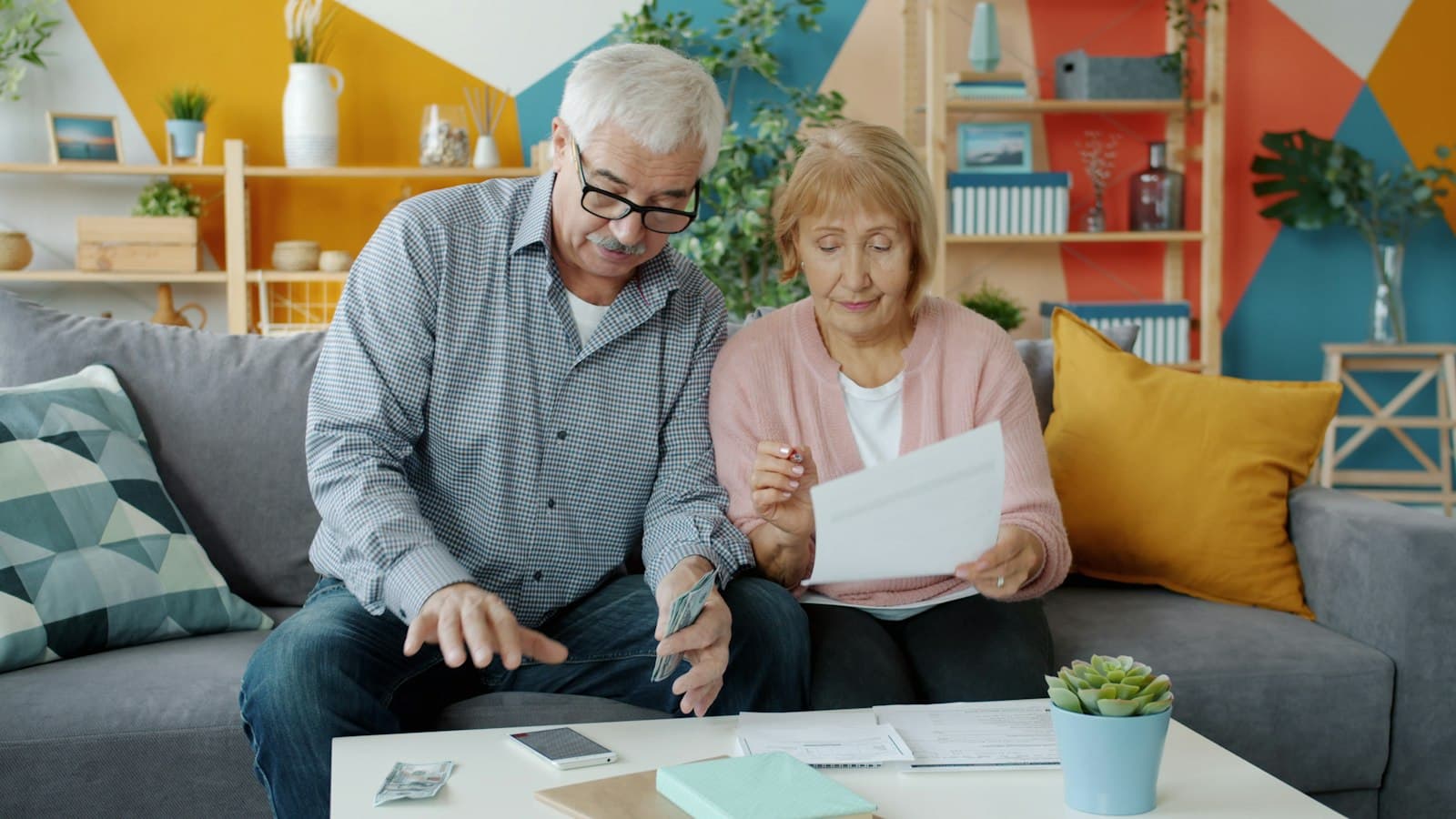 An older couple on a sofa reviewing household bills and cash together